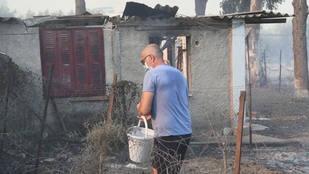 A man holds a bucket of water beside a house damaged by fire