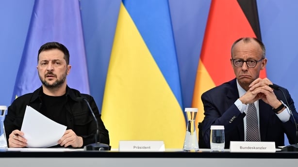 Two men sitting in front of German, Ukrainian, and European flags