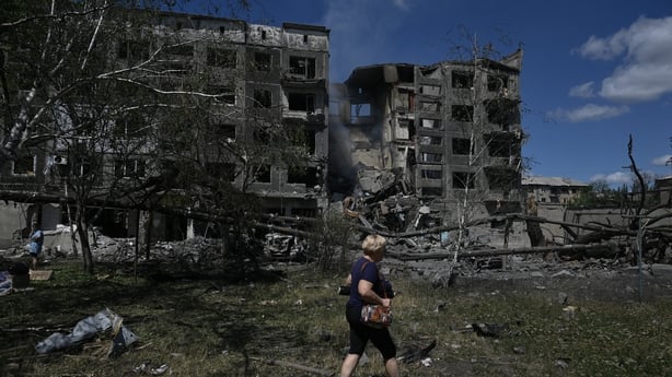 Woman on grass by a heavily-gutted multi-storey building which was destroyed by a Russian strike