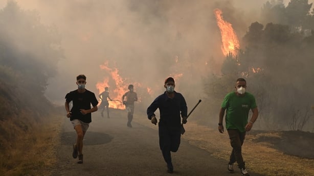 People run by a burnt area during a wildfire near the village of Larouco, in the province of Ourense, in northwestern Spain on August 13, 2025. Firefighters in Spain continue to battle fires across the country, where one volunteer has died while trying to extinguish a blaze, according to local autho