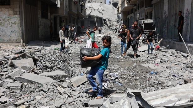 A young girl carries a plastic bag through rubble in Gaza