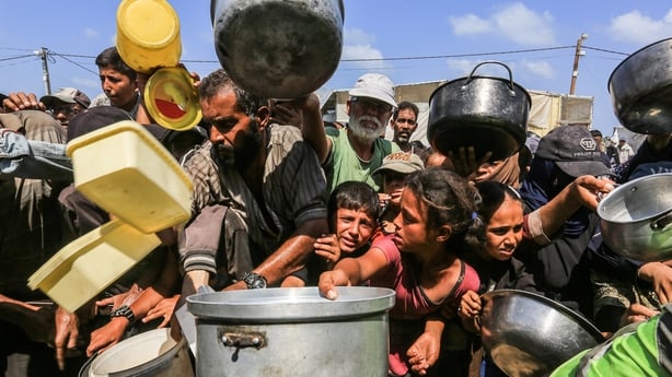 people crowd together, some crying, as they hold empty pots seeking food