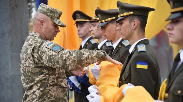 Several men in military uniform are seen folding a blue and yellow flag 