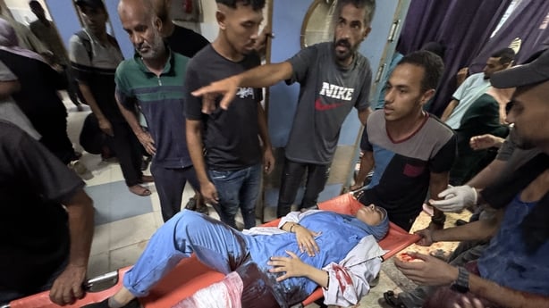 a woman wearing surgical scrubs with blood visible is carried out a stretcher at a hospital in Gaza
