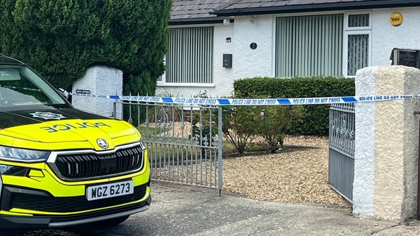 A police car in front of a house with a crime scene tape across the gateway