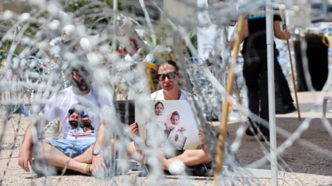 Reuters Lishay Lavi, the wife of hostage Omri Miran who was kidnapped in the deadly October 7, 2023 attack on Israel by Hamas, sits amid security wire during a protest to demand the release of hostages held in Gaza