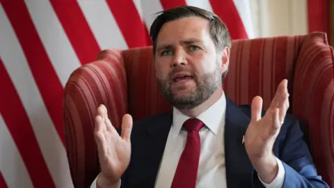 Reuters Vice-President JD Vance speaks during a meeting with UK Foreign Secretary David Lammy at Chevening House in Kent. He is sitting in a red armchair and gesturing with his hands.