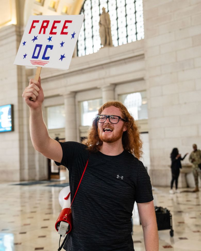 A protester holds a “Free DC” sign as Vice President JD Vance meets with members of the National Guard at Union Station.