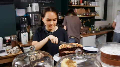 Getty Images A young women cuts a cake in a cafe - stock shot