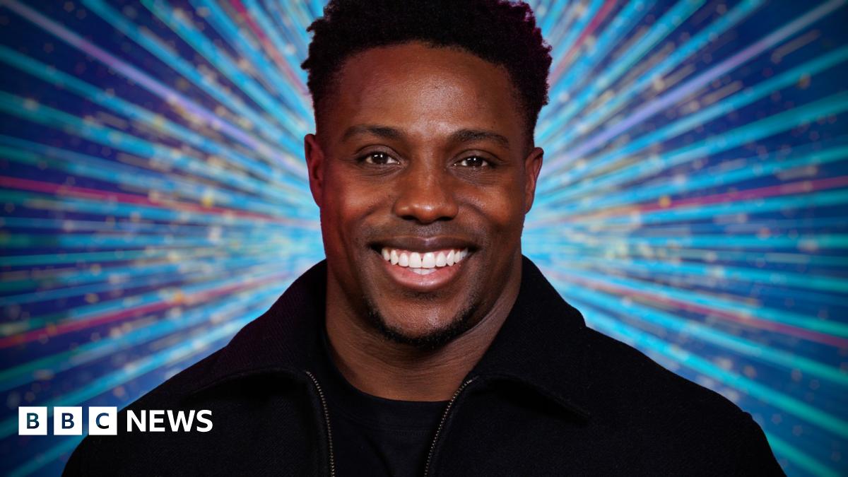 Harry Aikines-Aryeetey smiling in front of a multi-coloured glittery Strictly backdrop