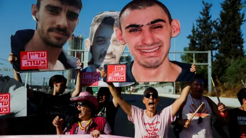 Reuters People hold photos of Israeli hostages and banners during a demonstration demanding an end to the Gaza war and the release of all the hostages held by Hamas, in Tel Aviv, Israel (19 August 2025)
