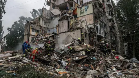 Getty Images Firefighters and rescuers sift through the rubble of a destroyed building