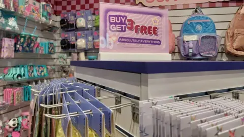 Grace Dean/BBC Items on sale at a Claire's store, next to a pink sign that says "Buy 3 get 3 free - absolutely everything"