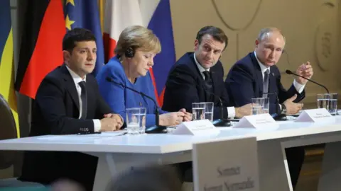 LUDOVIC MARIN/POOL/AFP via Getty Images Zelensky, Angela Merkel, Macron and Putin sit at a table at a summit
