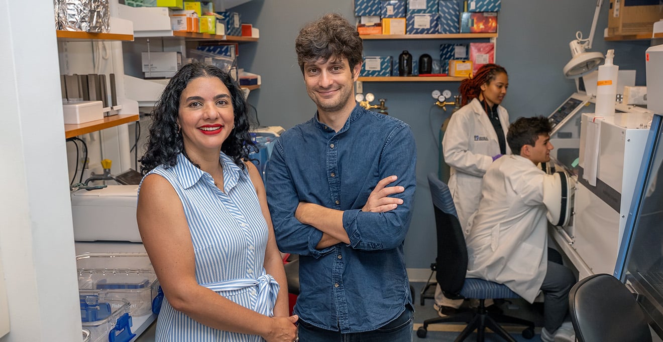 Ana Maldonado-Contreras, PhD; and Vanni Bucci, PhD, stand in the Maldonado-Contreras lab, with MD/PhD student Kairo Baylor and PhD student Hayden Gallo working behind the scenes.