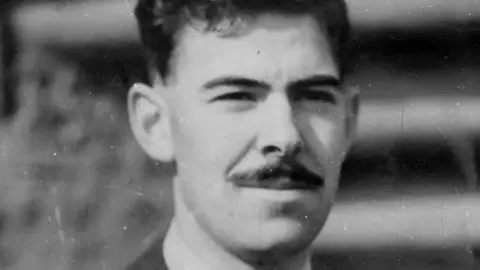 John Cruickshank A black and white picture of John Cruickshank staring just off camera. He has a dark moustache and dark hair. He is only visible from the neck up.