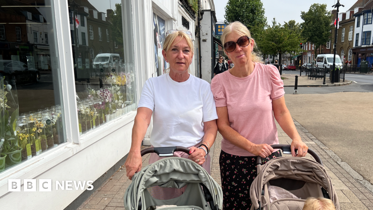 Two women with pushchairs pose for a photo on a high street.