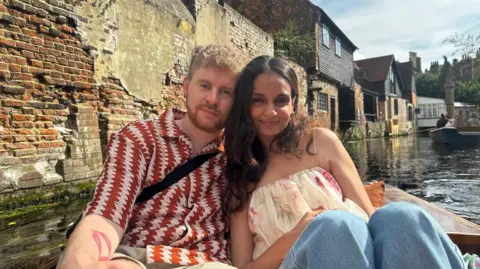 Conor Kehoe Conor Kehoe and Manisha Dev are sitting in a punt on a river smiling at the camera. He has wavy fair hair, a beard and moustache and is wearing a red and white patterned shirt. She has long, wavy dark hair and is wearing a floral top and jeans