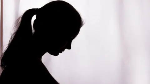 Getty Images A dark silhouette of a woman in profile with a ponytail, against a light background
