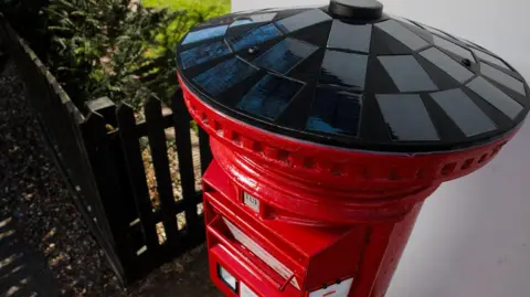 Royal Mail A view of black solar panels that cover the entire lid of the red postbox
 