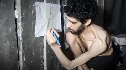 Other Evyatar David holds a pen and writes on a paper as he crouches, emaciated, in a tunnel in Gaza
