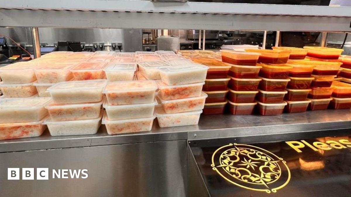 Dozens and dozens of tuppaware are stacked on a metal counter. The left half are filled with rice, the right half are filled with a red curry.