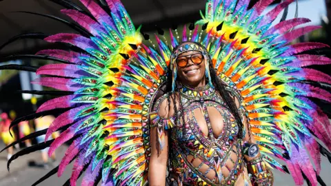 EPA A woman wears a rainbow coloured costume with feathers fanning out behind her.