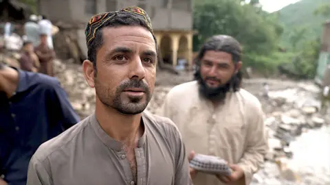 BBC A man wearing brown with another man in the background both standing on mud in Pakistan