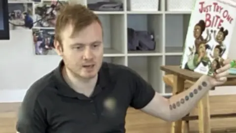 Supplied Joshua Dale Brown wearing black shirt, holding book at childcare centre 