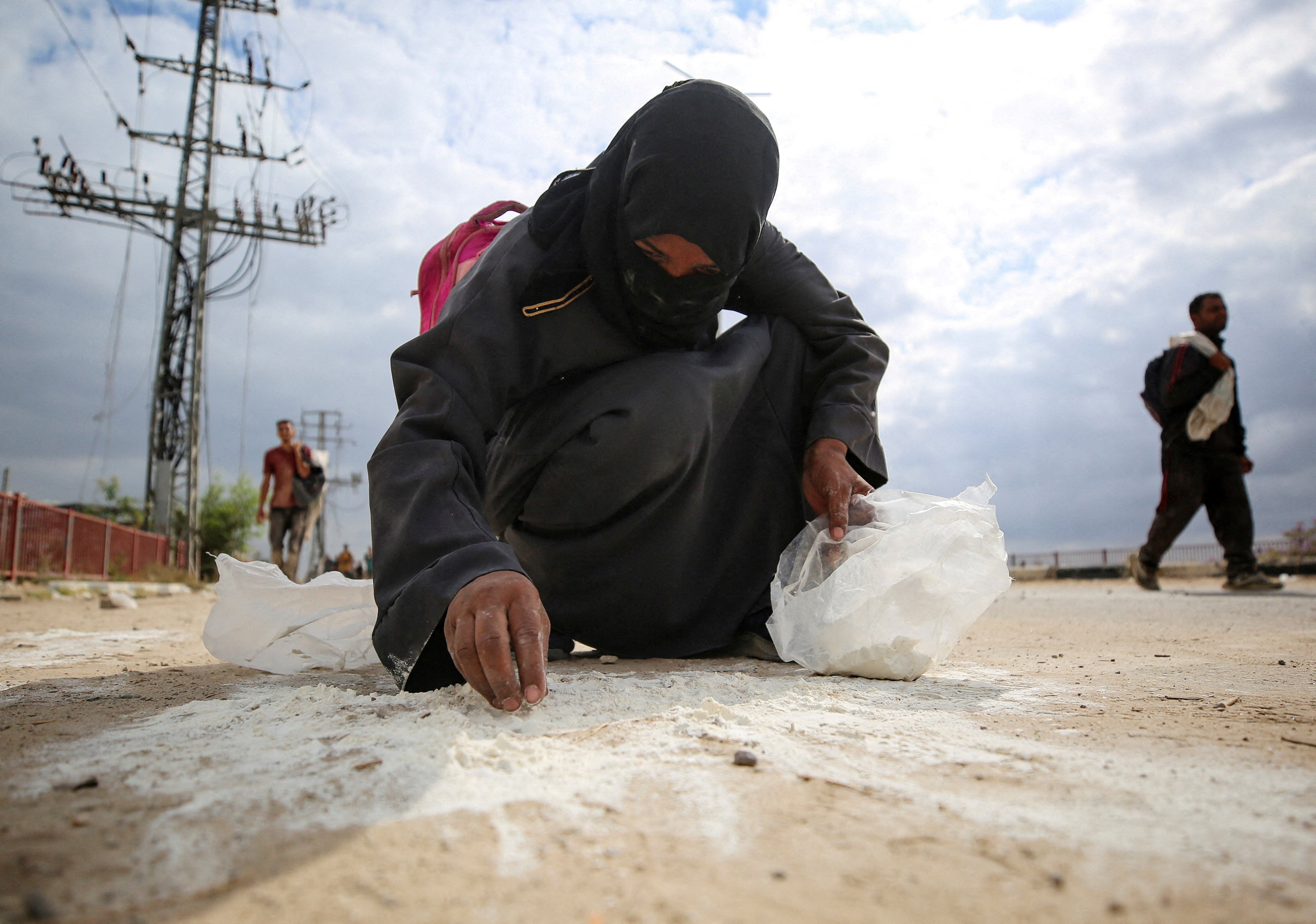 A woman collects flour from the ground as Palestinians receive aid supplies from the U.S.-backed Gaza Humanitarian Foundation (GHF)