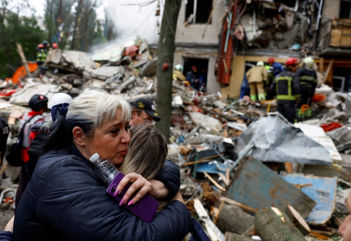 A woman embraces another woman in front of the site of an airstrike at an apartment building.