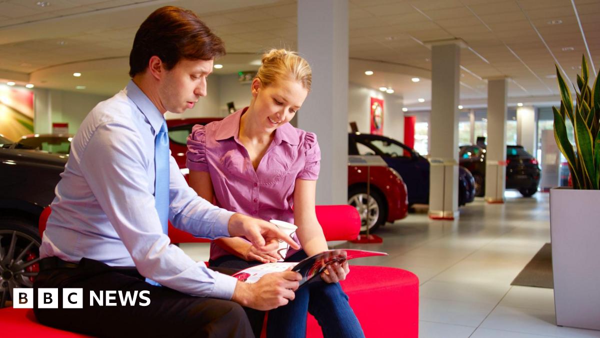 Sales representative with a young woman looking at paperwork in a car showroom