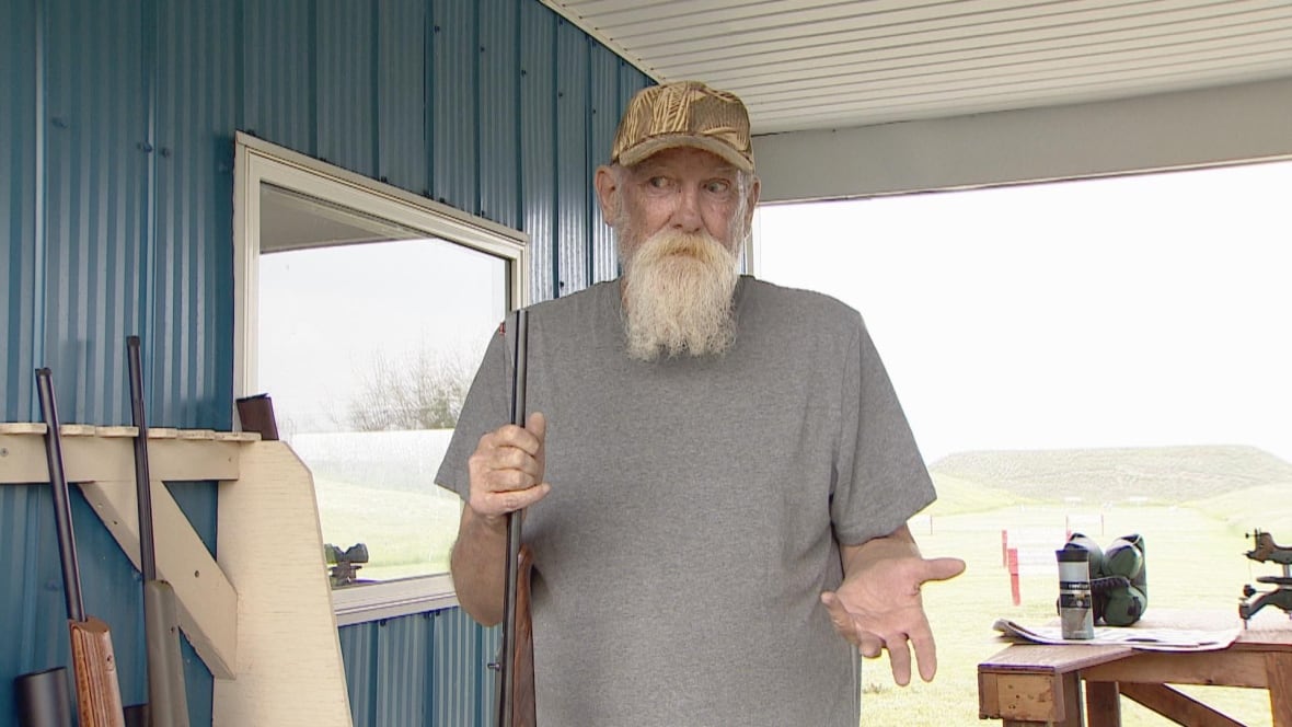 A man wearing a grey shirt gestures to the camera.