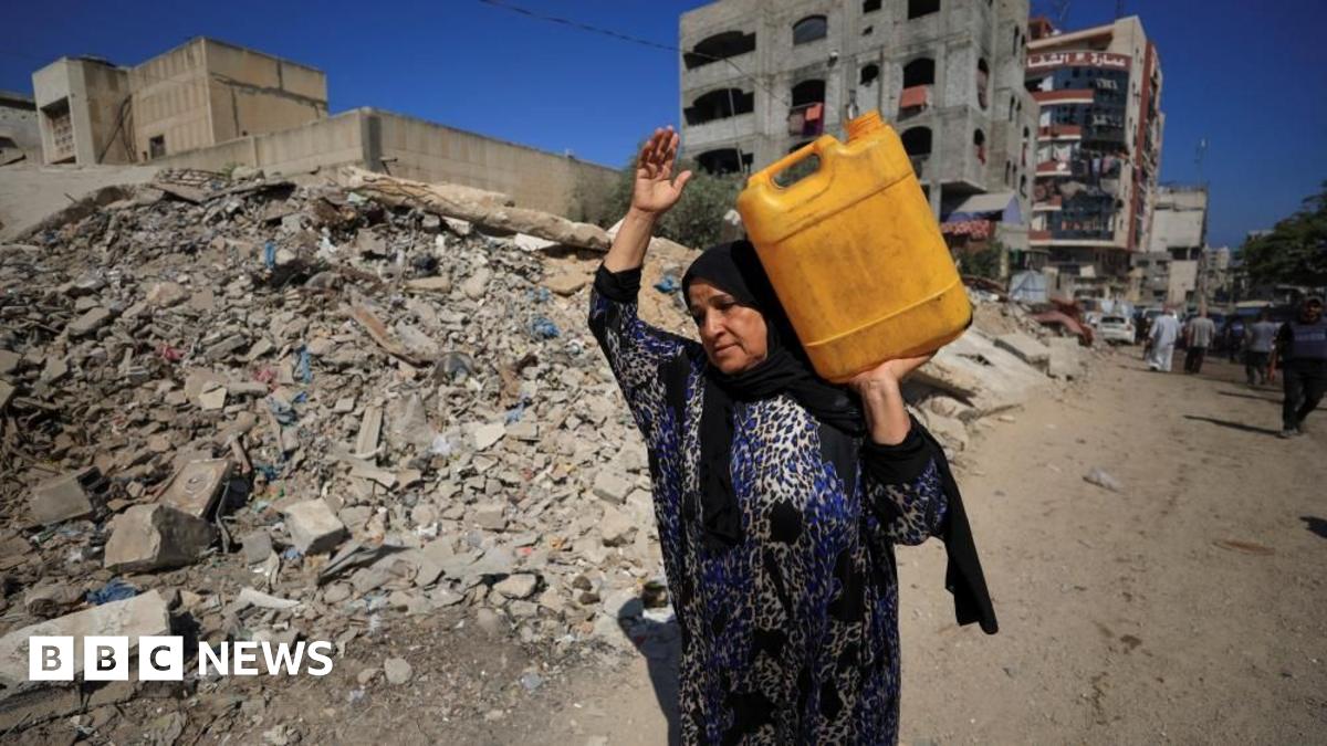 Palestinian woman carries a container of water as she passes by rubble in Gaza City (03/07/25)