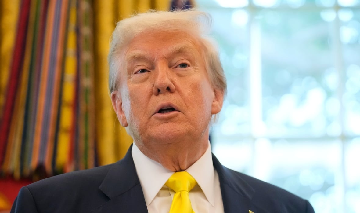 A man wearing a suit is shown from the shoulders up. His chin is tilted up and he appears to be in the middle of talking. 