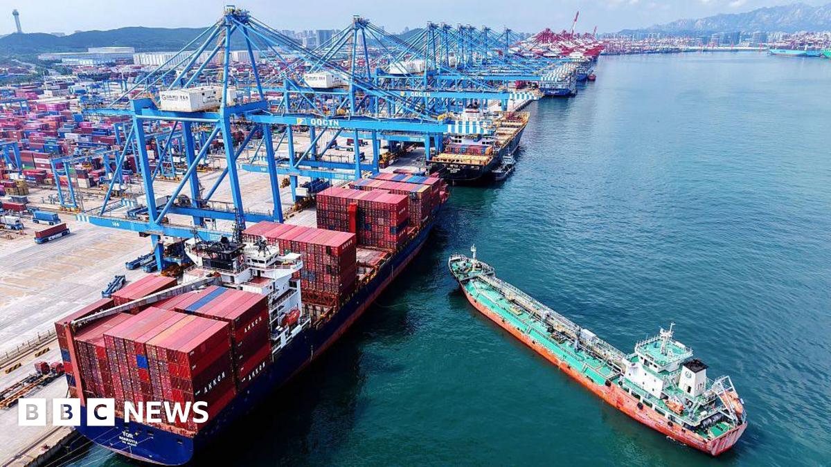 Aerial view of a container terminal in Qingdao with blue cranes hovering over container ships and a smaller green and orange boat approaching in east China's Shandong province Monday, 11 August, 2025.