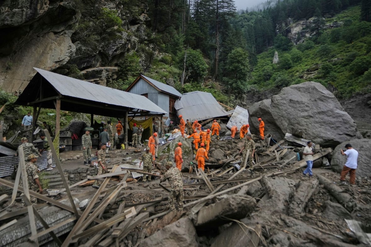 People in orange jumpsuits comb through wreckage in a mountainous region