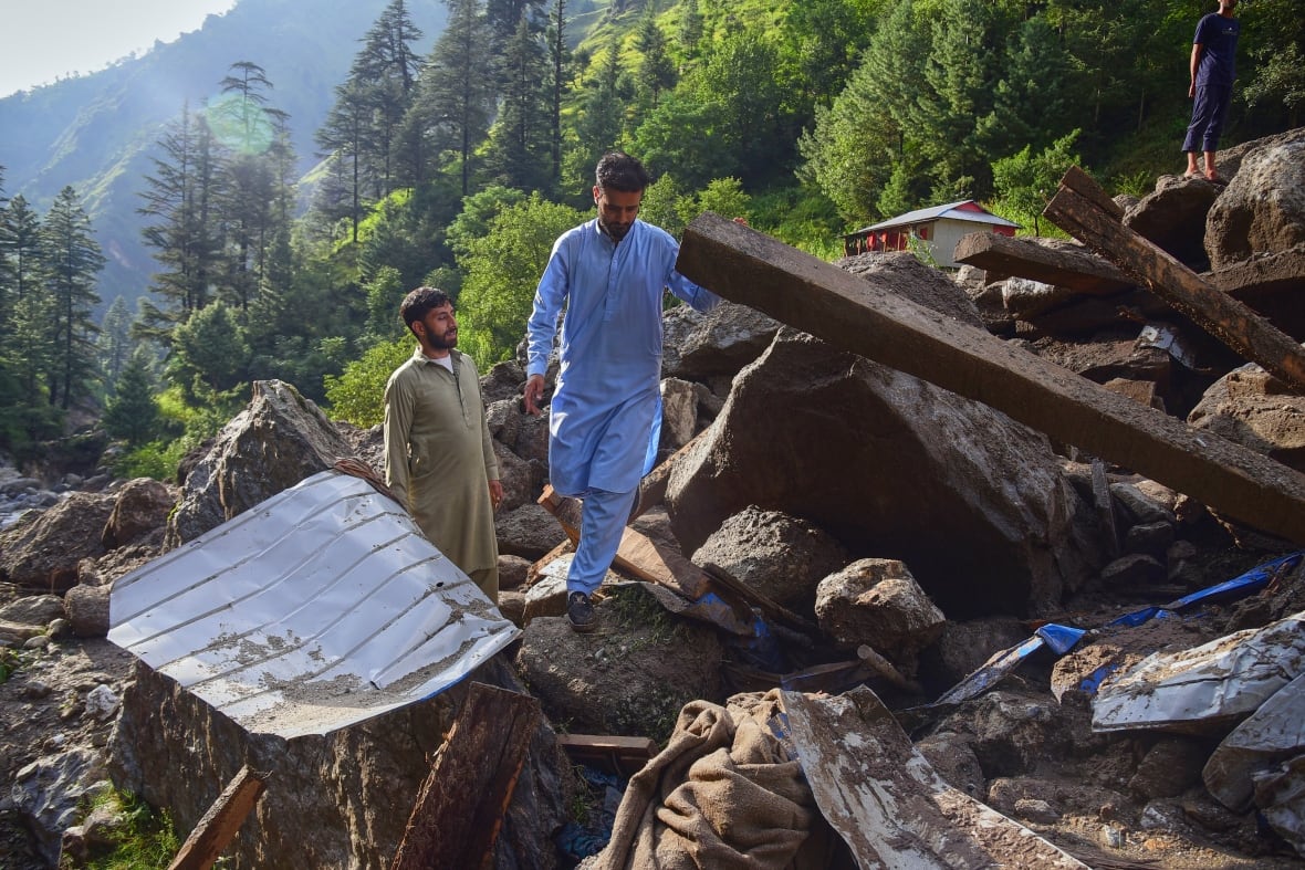 Two men walk through rubble and mud in a mountainous area
