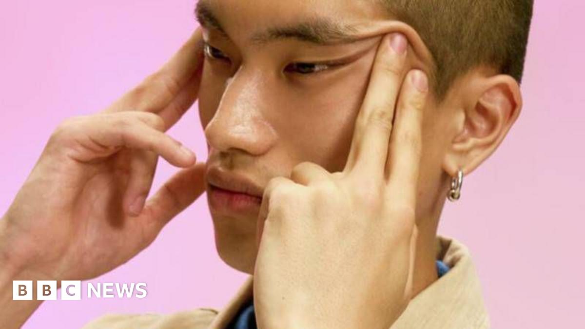 Close-up shot of a young Asian man with pulling the corners of his eyes up with both hands.