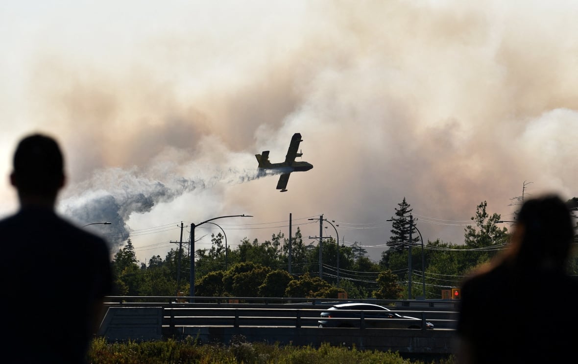 Two people in silhouette watching a water bomber fly by, releasing its load to fight a wildfire near Halifax.