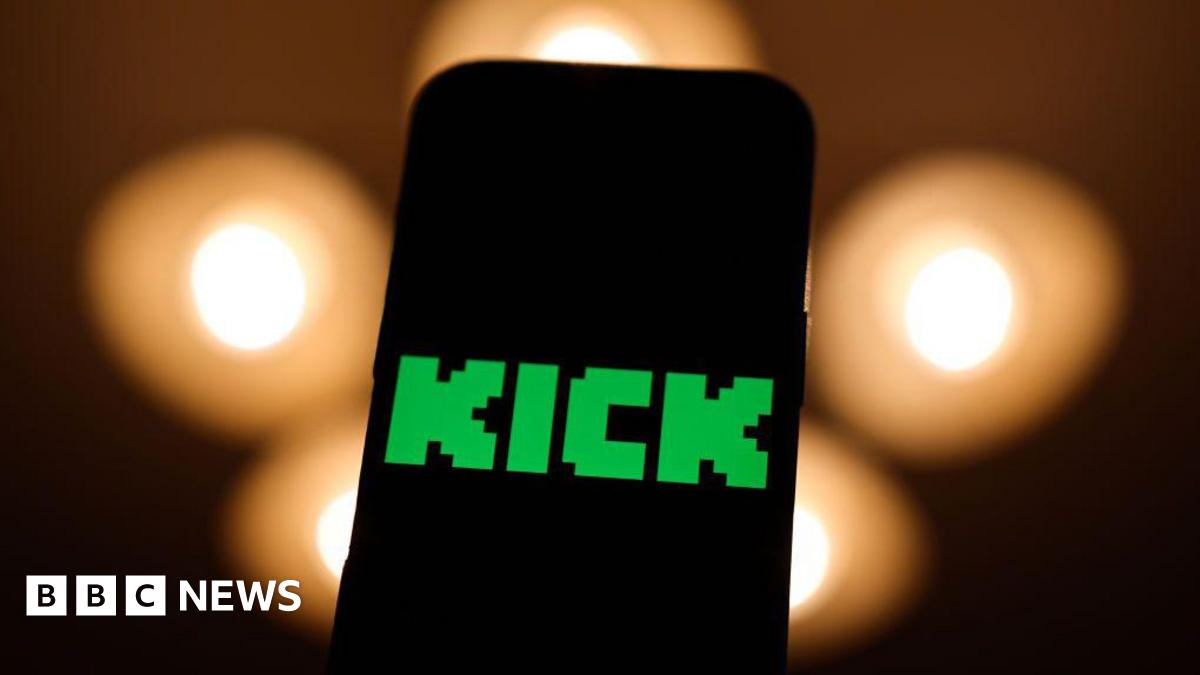 A phone screen with the Kick logo in green on it. Black background with orange blurry lights.