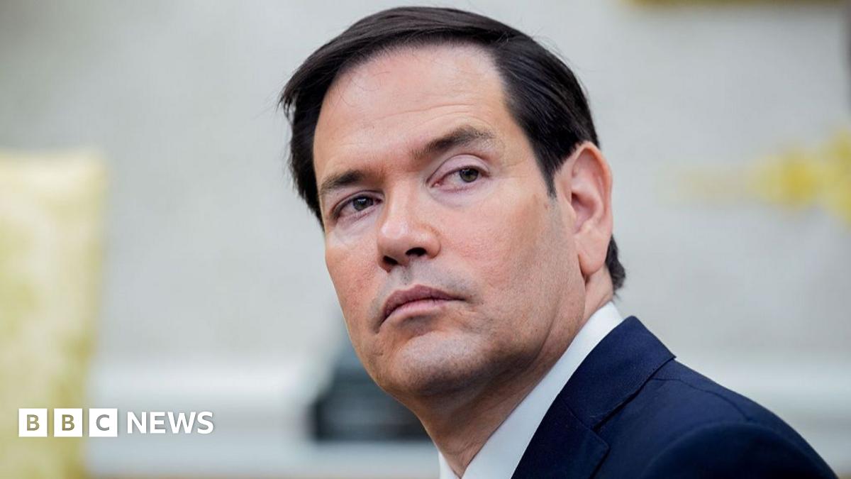 Francesca Albanese is wearing glasses and a dark-coloured top with a red and white scarf. She is looking to the left of the picture.