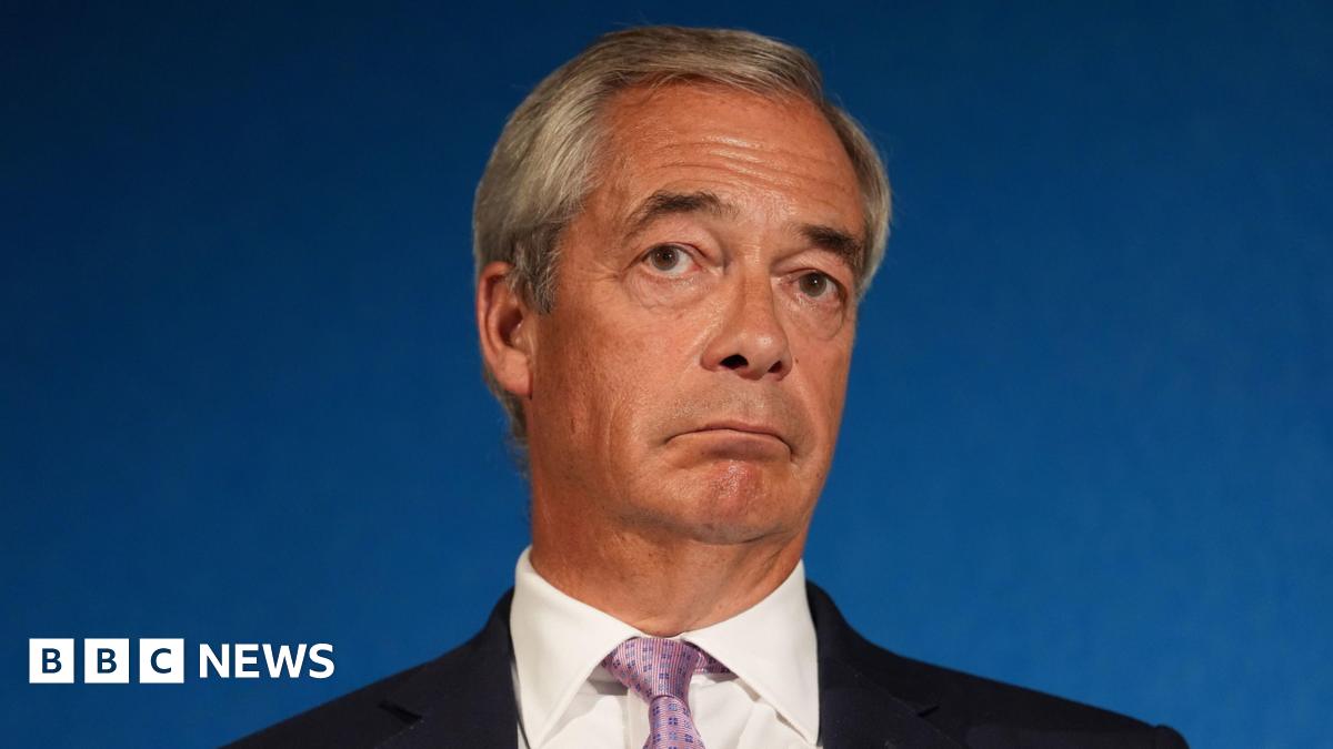 Reform UK party leader Nigel Farage looks stern at press conference, wearing a black suit jacket, white shirt and a pink tie.