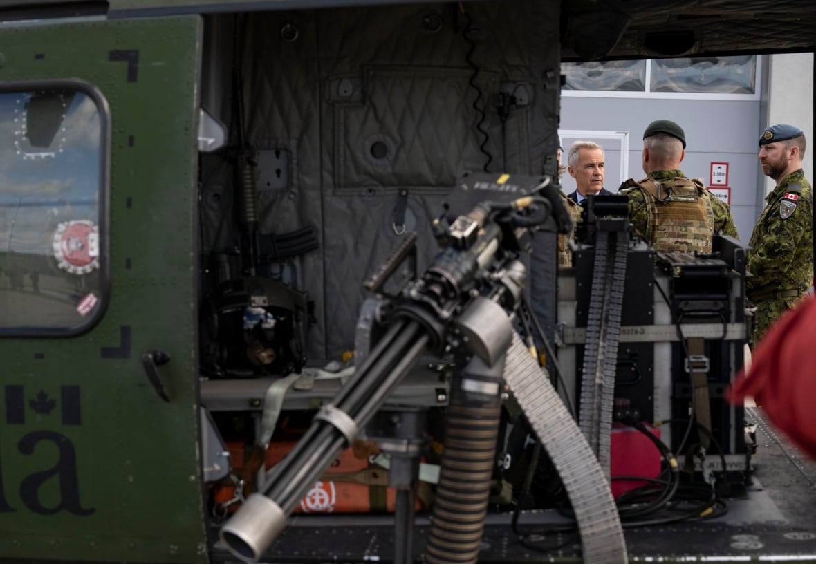 An armoured vehicle can be seen in the foreground, with a machine gun hanging out of it. Men stand behind it and seem to be in conversation.