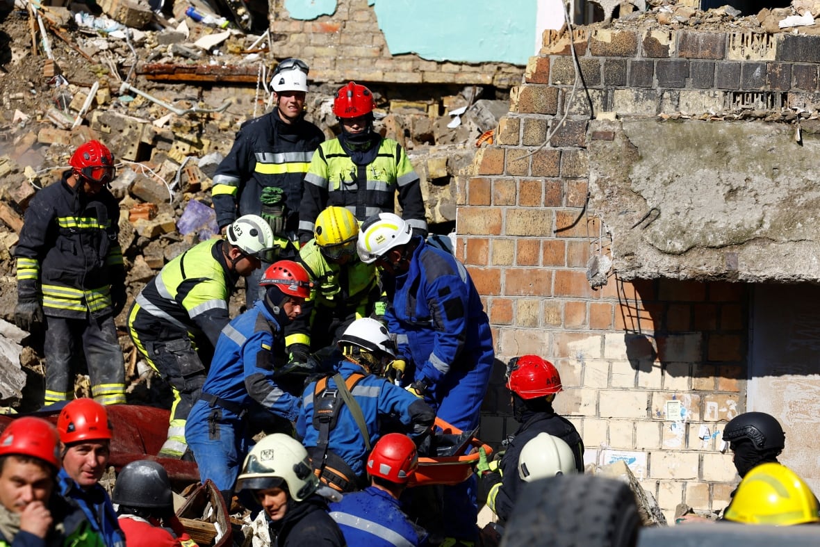 Rescuers in helmets move through rubble