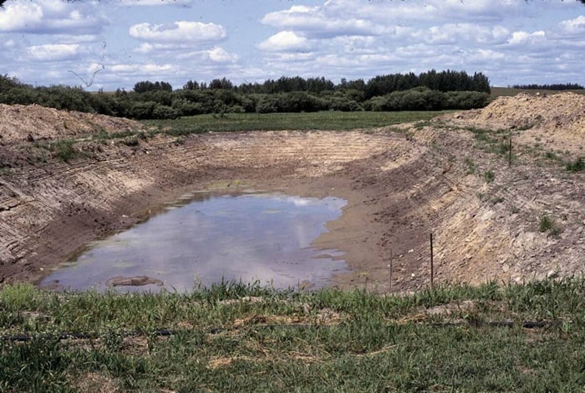 A photo of th low water level in a dugout on a summer day with scattered clouds.