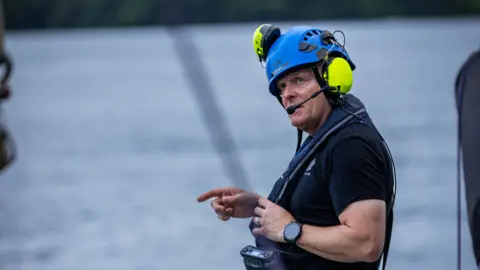 David Lochridge David Lochridge onboard the deck of a ship. He is wearing a headset and helmet - the sea in the background.  