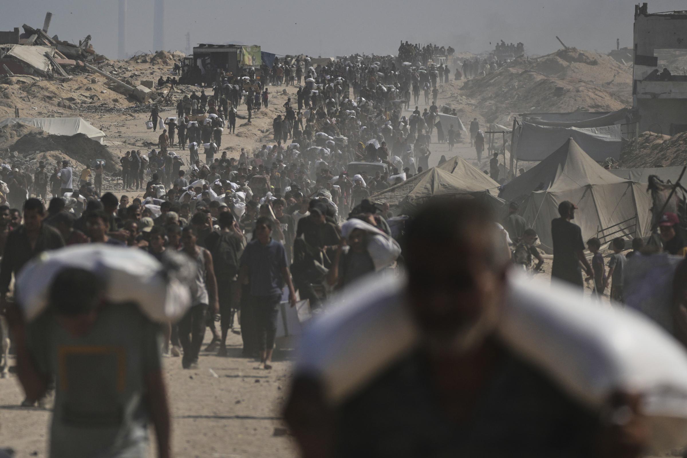 Palestinians carry sacks of flour unloaded from a humanitarian aid convoy on the outskirts of Beit Lahiya, northern Gaza Strip, Saturday, Aug. 23, 2025. (AP Photo/Abdel Kareem Hana).