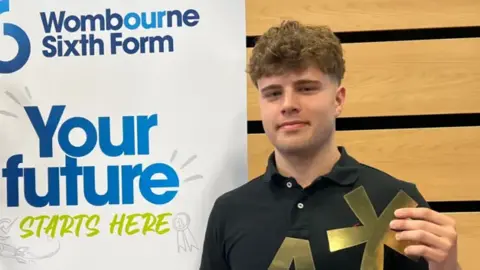 Boy smiling at camera in front of a sixth form school banner