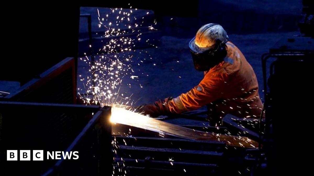 A steelworker in full protective gear working at a steel plant. Sparks are flying as he appears to cut through a material